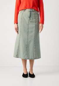 Lys blå denim midi skjørt med vertikale sømmer, front knappelukking og en tettsittende midje. Brukt med svarte flate sko.