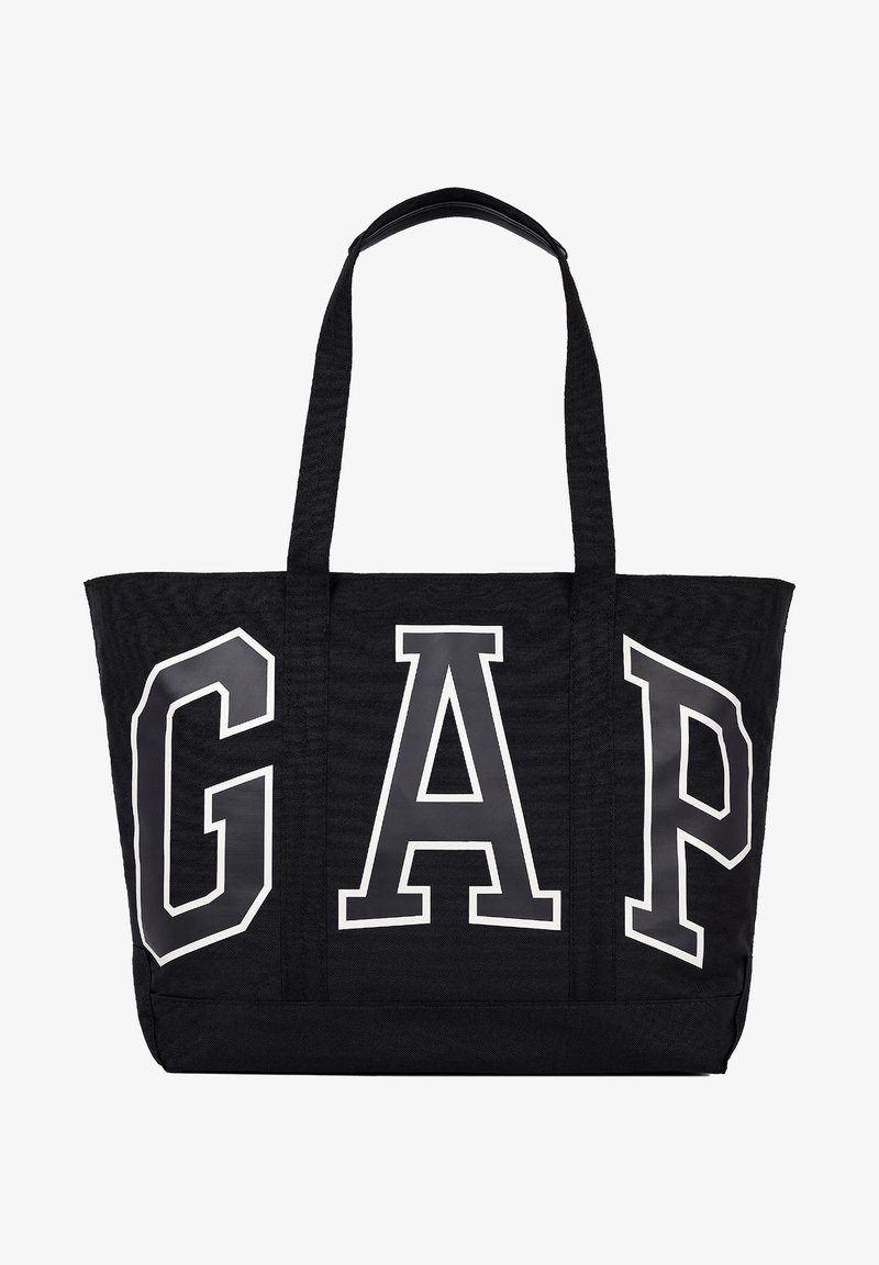 Sac fourre-tout noir avec de longues anses et de grandes lettres blanches contours formant le mot GAP sur le devant.