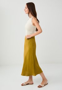 Top bez rękawów w kremowym kolorze w połączeniu z lejącą się spódnicą w kolorze musztardowym do kolan. Sandały na białych paskach. Prosty i elegancki design.