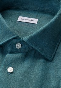 Chemise texturée bleu sarcelle avec col boutonné et étiquette blanche portant l'inscription « seidensticker » à l'intérieur du col.