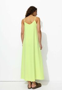 Robe longue et ample en tissu vert néon avec de fines bretelles et un dos en V, offrant une texture lisse et respirante.