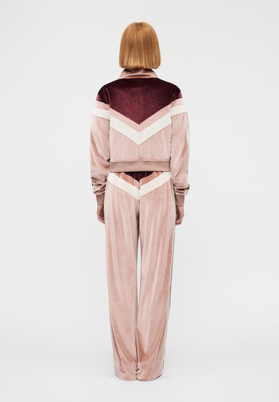 Βελούδινο σετ φόρμας σε αποχρώσεις του ροζ και του μπουρντό, με σχέδια ψαροκόκαλο και παντελόνια με φαρδιά μπατζάκια, με ριμπ μανσέτες και λεπτομέρεια στον γιακά.