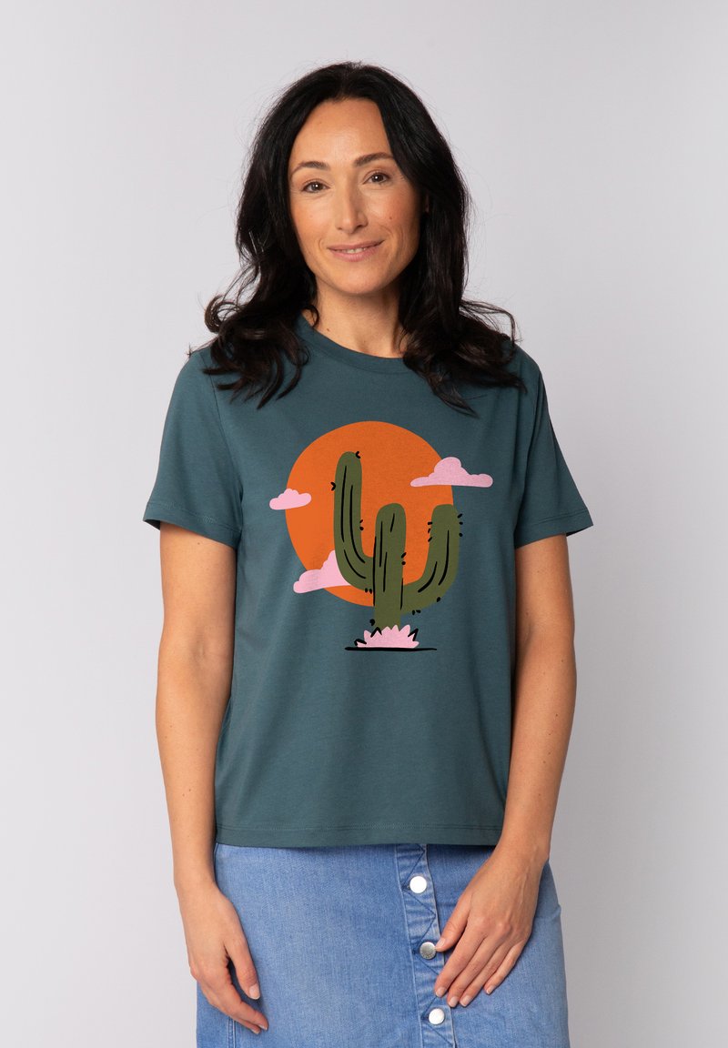 Teal Baumwoll-T-Shirt mit einem Kaktus-Graphic, einem orangefarbenen Kreis und rosa Wolken. Klassische Passform mit kurzen Ärmeln, glatte Textur.