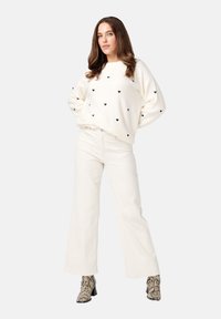 Witte pullover met zwarte hartpatronen, gecombineerd met witte wijde broek en enkelboots met slangenprint, in een relaxed fit.