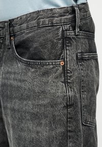 Κοντινό πλάνο στην περιοχή της τσέπης γκρι τζιν με όξινη πλύση, με ορατή θηλιά ζώνης και λεπτομέρειες από χαλκό.