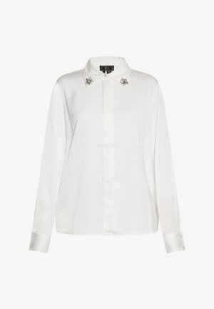 Valge siidine pluus klassikalise krae ja kaelakaunistusega, samuti nööbitud varrukate mansettidega, millel on dekoratiivsed kristallaktsendid, valmistatud voolava silueti saavutamiseks.