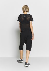 Schwarzes cropped Top mit Mesh-Textur, kombiniert mit lockeren schwarzen Harem-Hosen. DieFootwear zeigt eine Kombination aus Grau und Schwarz. Einfaches Design.