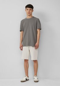 T-shirt gris à manches courtes avec un col rond, associé à un short beige clair. Le t-shirt présente un petit logo sur la poitrine.