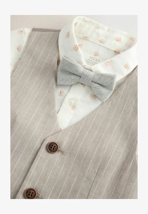 Grijs gestreepte vest met bruine knopen, gecombineerd met een wit shirt met een teddybeerpatroon, aangevuld met een grijze vlinderdas.