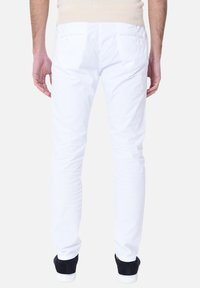 Pantaloni in cotone bianchi con una vestibilità slim, dotati di tasche posteriori e dettagli di cucitura sottili, abbinati a scarpe sportive scure.