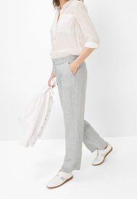 Pantalon en lin gris clair avec ceinture élastique, poches latérales et coupe décontractée, associé à une chemise blanche boutonnée et des baskets blanches.