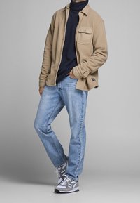 Beige mikina z fleece s kapsou na prsou, námořnický rolák, světle modré džíny a šedé sportovní boty s bílými akcenty.