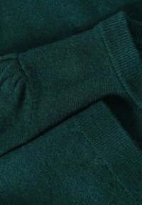 Tissu tricoté vert foncé avec poignets côtelés, montrant de près la texture et les plis d'un pull ou d'un vêtement similaire.