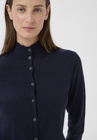 Tengerészkék bordázott kötött kardigán magas, hullámos gallérral, elöl hat textilgombbal és hosszú ujjal.