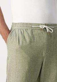 Light green elastic-waist pants made of breathable fabric, featuring a drawstring with gold accents and side pockets. Smooth texture.