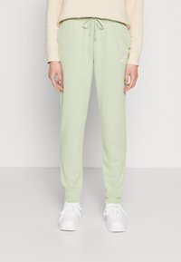Pantalones de chándal verde claro con cintura ajustable, hechos de material suave, con un pequeño logo blanco de Nike en el lado izquierdo.