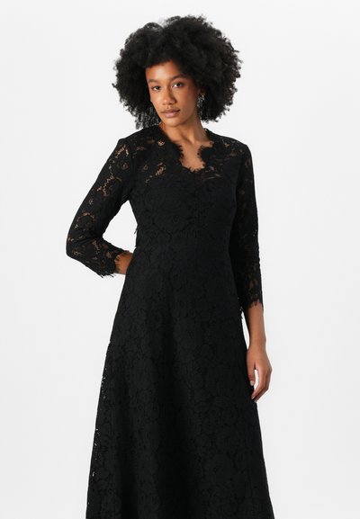 Robe en dentelle noire avec un corsage ajusté, décolleté festonné et manches longues. Présente des motifs floraux et une jupe fluide.