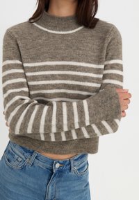 Strikket sweater i lysebrun med hvide vandrette striber, med en ribbet høj hals og lange ærmer, lavet af et blødt, tekstureret materiale.