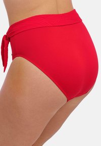 High-waisted red swim bottoms made from smooth fabric, featuring a textured waistband with a tied accent and a seamless finish on the legs.