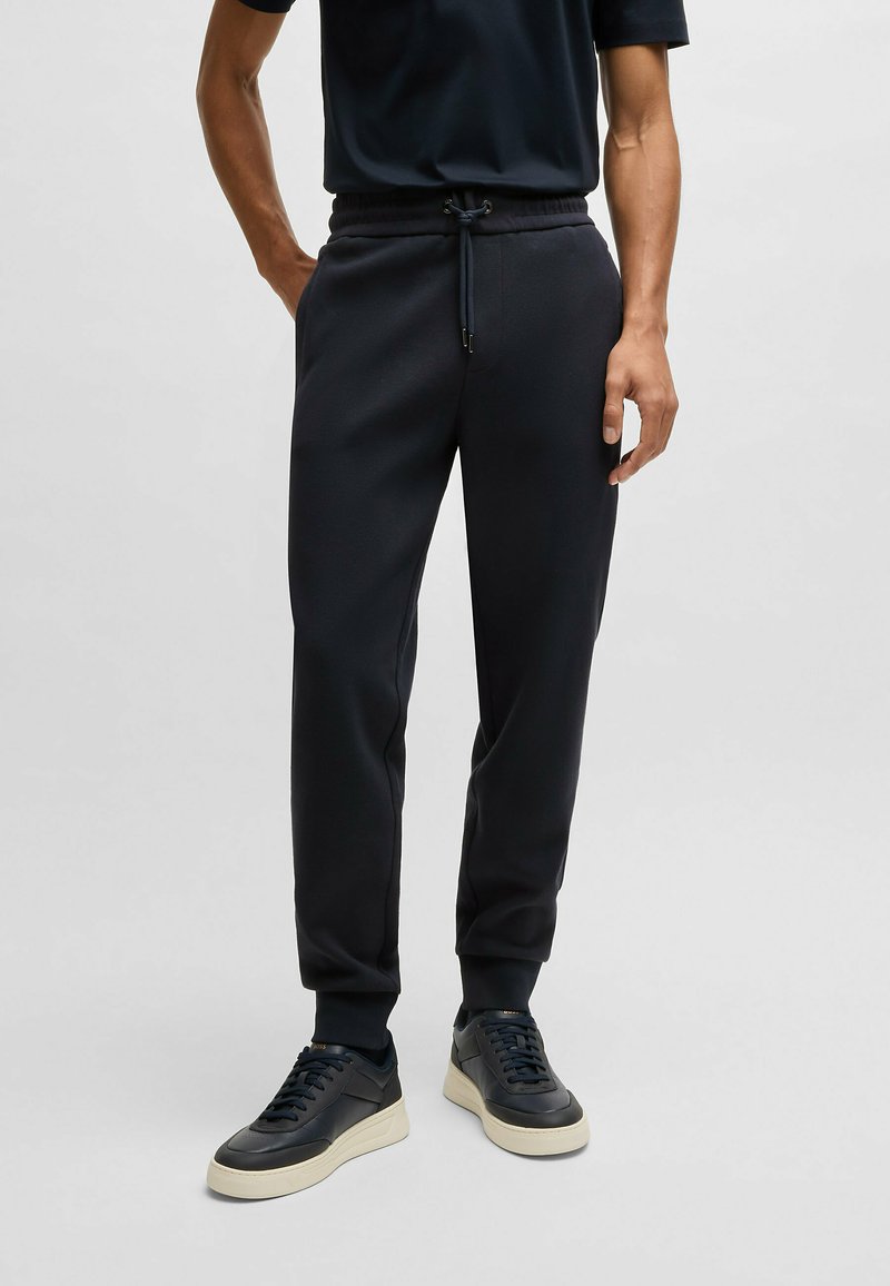 Svarta sweatpants med resår i midjan och dragsko. Tyget ser slätt ut. Kombineras med mörka sneakers som har en krämfärgad sula.