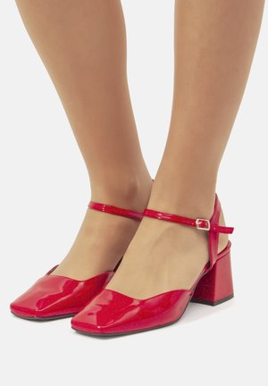 Scarpe con tacco blocco in pelle verniciata rossa, con design a punta quadrata e sottile cinturino alla caviglia dotato di fibbia metallica. Texture liscia e finitura lucida.