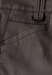 Pantalones de tela gris con un bolsillo frontal con herrajes negros, costuras visibles y una textura suave. El diseño incluye detalles de pasadores para el cinturón.
