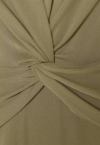 Olivově zelená tkanina s texturovaným pletením, obsahující nařasené části a design s otočením ve středu, který zvýrazňuje její splývavý vzhled.