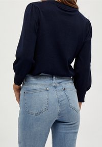 Granatowy sweter z bufkami w połączeniu z jasnoniebieskimi dżinsami o wysokim stanie, które mają dwie tylne kieszenie i minimalne detale metalowe.