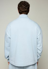 Lyseblå oversized sweatshirt med høj krave, der har en blød tekstur og ribbede manchetter. Glat stof og minimal sømad.