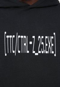 Μαύρη κουκούλα με λευκό κείμενο που αναγράφει "[ttc/CTRL-Z_25.EXE]" κεντραρισμένο στο στήθος.