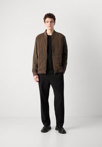 Brown insulated bomber jacket with ribbed cuffs and hem, paired with black straight-leg trousers and black lace-up shoes.