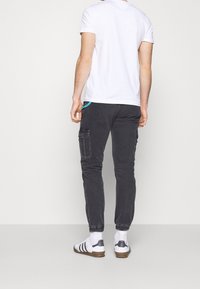 Pantalones cargo negros con puños elásticos, bolsillos laterales y un acento verde. Combinados con una camiseta blanca y zapatillas deportivas blancas.