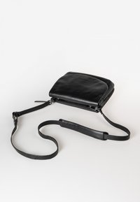 Schwarze Leder-Crossbody-Tasche mit flachem Design, Reißverschluss, verstellbarem Tragegurt und dezentem Logodetail auf der Vorderseite. Glatte Textur.