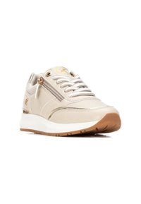 Zapatilla beige con parte superior texturizada, acentos metálicos, detalle de cremallera y suela blanca acolchada. Cintas planas y suela de goma.