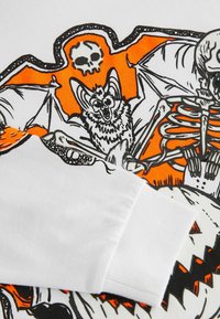 Valge särk, millel on värvikas oranž ja must graafiline disain, kus on skeleton, nahkhiired ja kolju. Puuvillane materjal ribadega varrukaotsadega.