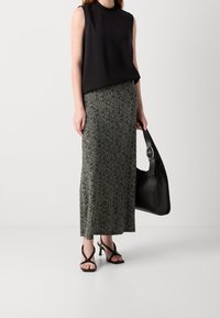 Blouse noire sans manches associée à une jupe maxi à motifs en crème et noir. Tenant un grand sac à main noir avec un accent circulaire.