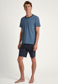 Kortebloemige blauwe t-shirt met een zwarte ronde hals en zak, gecombineerd met donkerblauwe shorts. Gladde textuur, casual pasvorm.
