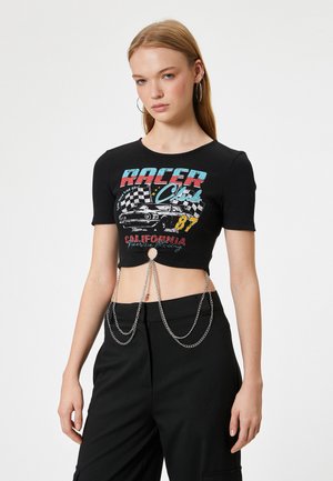 Zwarte geribbelde crop top met kleurrijke "Racer Club" grafiek, met kettingdetails die hangen vanaf een centrale cirkelvormige uitsnede aan de onderrand.