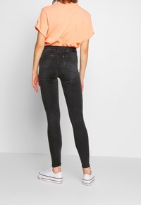 Svarta tajta jeans med hög midja, bakfickor och subtila blekningar. Kommer med en klar orange t-shirt och vita sneakers.