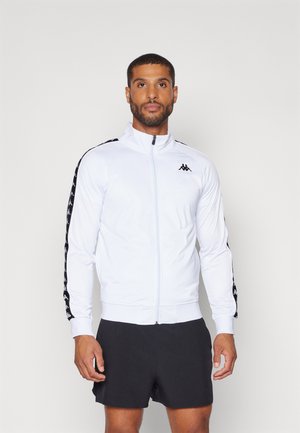 Chaqueta blanca con cremallera y detalles en negro, con un corte ajustado, mangas largas y un patrón de rayas en contraste a lo largo de las mangas.
