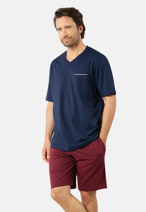 T-shirt bleu marine à col en V avec une poche blanche, associé à un short bordeaux à petits pois blancs. Tissu lisse, coupe décontractée.
