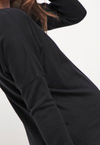 Maglione nero a maniche lunghe con vestibilità rilassata, caratterizzato da un ampio scollo e una texture morbida. Il tessuto appare leggero e confortevole.