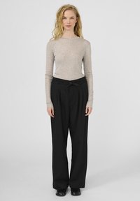 Lichtgrijze longsleeve top met een ronde halslijn, gecombineerd met zwarte high-waisted wijde broek met een strikband en plooien.