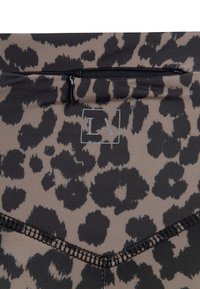 Leggings con stampa animale nei colori nero e beige, dotati di una tasca con zip e di cuciture in contrasto nere lungo le cuciture.