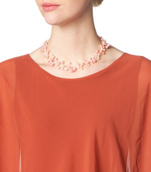 Collana di perle con perle di diverse dimensioni in rosa e crema, disposte in modo intricato, su un top di tessuto arancione leggero.