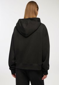 Czarna, oversize bluza z miękkiej tekstury, z kapturem na sznurku, szerokimi rękawami oraz ściągaczami w mankietach i u dołu. Minimalistyczny design.