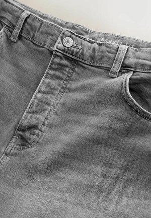 Pelēkas džinsa bikses ar pogu, uz kuras rakstīts "Premium Denim Goods", redzamas jostas cilpas, priekšējā kabata un uz jostas iekšējās malas teksts "BARREL FIT".