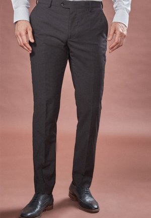 Pantalones negros de corte ajustado con una textura suave, corte recto y cierre de botón. Llevados con zapatos de vestir negros, exhibidos sobre un fondo neutro.