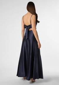 Navy Satin Abendkleid mit tailliertem Oberteil, dünnen Trägern und einer großen Schleifen-Applikation auf der Rückseite, die in einen langen, plissierten Rock übergeht.
