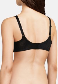 Donna che indossa un reggiseno nero a fantasia visto da dietro, con spalline regolabili e chiusura a gancio.